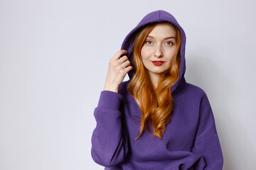 A redhead woman in a purple hoodie adjusts the hood. White background