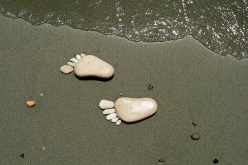 Two stone footprints on beach sand beside sea wave