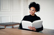 © muse studio - In the college library. Reading holding a book textbook white cover blank. The student is a smart African American looking woman.