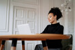 © muse studio - A satisfied female student designer smiles at an Afro-ethnic appearance. In the browser, working on a new work project. The freelancer works remotely on a laptop. Curly black hair.