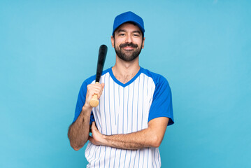 Wall Mural - Young man playing baseball over isolated blue background keeping the arms crossed in frontal position