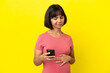 © luismolinero - Young mixed race pregnant woman isolated on yellow background using mobile phone