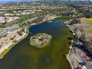 a stunning aerial shot of the vast green and blue lake water with lush green and yellow plants on the hillside with miles of homes and lush green trees and blue sky at Laguna Niguel Regional Park