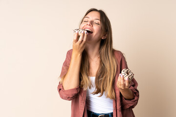 Young Lithuanian woman isolated on beige background eating a donut