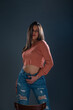 © qunica.com - Female model with an orange crop top blouse and jeans posing in front of a wooden chair