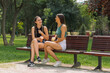 © qunica.com - Close-up of two young girlfriends sitting on a bench in summer park chatting and having fun