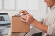 © Daniel - Smiling man wearing glasses unpacking awaited parcel, looking inside, sitting at work desk, satisfied happy customer opening cardboard box with online store order, good shipping delivery service.