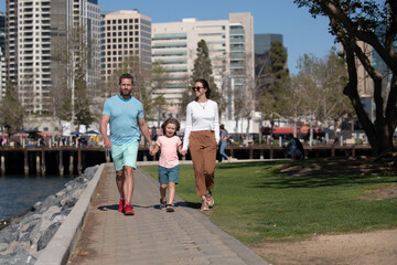 Wall Mural - Portrait of happy young family walking with their child on the city. People urban concept. Mother, father and kids on vacation on background of skyscrapers in San Diego.