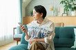 © One - リビングでスマートフォンを見る女性