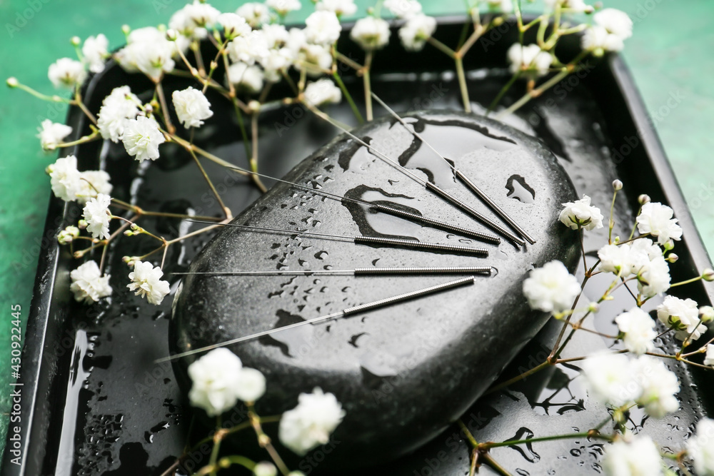 Acupuncture needles, spa stone and flowers on stand