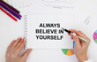 © Veranika - The girl holds a notebook with the text ALWAYS BELIEVE IN YOURSELF, next to reports and diagrams, pencils.