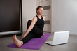© Aleksandra Iarosh - young woman doing asana at home on yoga mat in front of laptop
