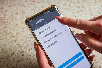 Male thumb finger over parcel delivery app on smartphone screen