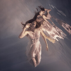 Wall Mural - A girl in a white dress with long dark hair swims underwater as if floating in weightlessness