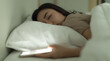 © Bangkok Click Studio - Cute young Asian woman laying on the bed while holding the switch on an open light smartphone in hand and asleep, nap with tired and deep sleep. Social media addict concept.