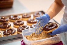 A Worker Sprinkles Ground Hazelnuts Over Donuts In A Candy Workshop. Pastry, Dessert, Sweet, Making