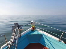 A Photograph In The Prow Of A Small Blue Fishing Boat Slowly Sailing Through The Sea. You Can See Anchor Made Of Iron And Equipment Used To Worship Sacred Objects And The Calm Sea In Front.
