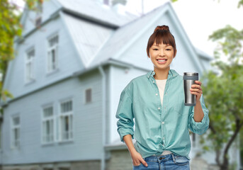 Wall Mural - sustainability and people concept - portrait of young asian woman in turquoise shirt with thermo cup or tumbler for hot drinks over living house background