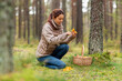© Syda Productions - picking season, leisure and people concept - young asian woman with basket and knife cutting chanterelle mushroom in autumn forest