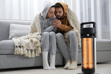 Canvas Print - Young couple getting warm near electric heater at home