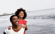 Black mother and daughter running on the beach at sunset time during summer vacation - Focus on mother face