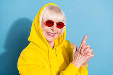 Wall Mural - Photo of cheerful nice positive old woman wear hood sunglass hold fingers gun isolated on blue color background