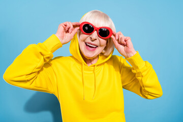 Sticker - Photo of attractive nice old woman wear sunglass hood good mood smile isolated on blue color background