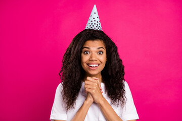 Poster - Photo of grateful curly young party lady hold hands wear cap white t-shirt isolated on pink color background