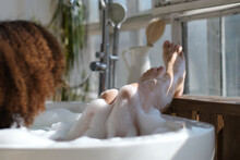 Back View Curly Black Girl Laying, Relaxing In The Bath Indoors. Young Woman Relaxing In Warm Bathtub With Foam And Bubbles. Tired Female Enjoying Rest Pamper Herself.
