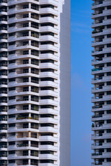 Sunlight and shadow on surface of balconies and terraces of 2 high residential buildings against blue sky background in vertical frame