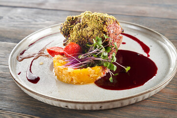 Wall Mural - Tasty meal with fruits, berries and sprouts presented on ceramic white plate in luxurious restaurant. Close up view of beef meat with pistachio topping served with cranberry sauce on wooden table.