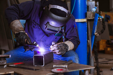 Welder is welding the steel in the factory. Weld the steel in dark. Workers wearing industrial uniforms and welding masks at a welding factory protect from welding sparks. Occupational safety concept