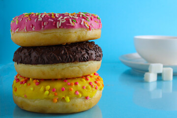 Wall Mural - Still life donuts yellow pink yellow chocolate and a cup of tea coffee in the background on a blue bright background. a day without diets. poster to the kitchen