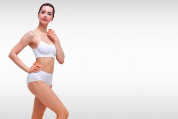 Wall Mural - Beautiful slim woman in white lingerie against a grey background with copyspace