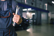 The hand of a car repairman with keys and a special tool on the background of the service area. A mechanic in a car service station in uniform. Copy space