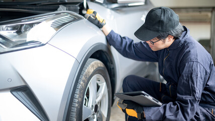 Asian auto mechanic holding digital tablet checking car wheel and tire in auto service garage. Mechanical maintenance engineer working in automotive industry. Automobile servicing and repair concept