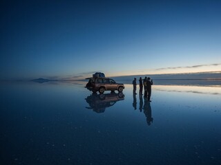 Wall Mural - Tourist group with offroad car SUV on Salar de Uyuni salt flat lake in Bolivia andes mountains sunrise mirror reflection