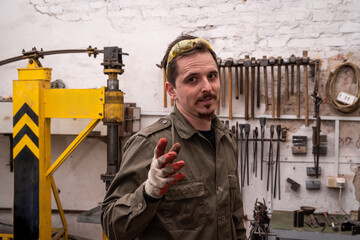 Wall Mural - Portrait of a blacksmith against the background of machines and tools. The man is gesturing, looking at the camera.