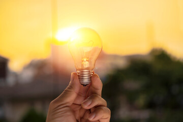 Wall Mural - hand holding a light bulb with sunset power
