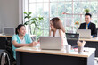 © Avirut S. - Young disabled woman sitting on wheelchair using computer to discuss project with her female colleagues. Business people on wheelchair in the office. Business Woman talking with disabled colleague.