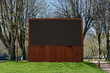 Public open-air media screen in the park decorated with iron sheets with rust effect on the background of trees and green grass. Stylized advertising and information media construction in the park