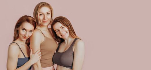 Wall Mural - three girls in comfortable home clothes together on a pink background. women smile and have fun. the