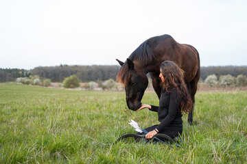 Wall Mural - beautiful woman kneeling on the ground in her hand with a bow and a horse has her head near her