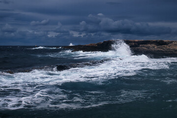 Wave crashing against rocks on a beach in Qawra, Malta on a stormy day.