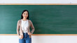 © JR-50 - Portrait of a young Asian teacher smiling happily in front of the classroom. Close up women student looking at camera on blackboard. back to school concept