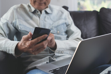 Poster - Man wearing casual clothes sitting on sofa using mobile phone browsing the internet and laptop computer working from home