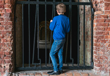 A Small Boy Stands At The Bars On The Casemates
