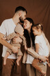 © Ananass - A young sincere family where a stylish bearded father and a cute wife hold their cute children in their arms. Family photo shoot in the studio