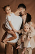 © Ananass - A young sincere family where a stylish bearded father and a cute wife hold their cute children in their arms. Family photo shoot in the studio