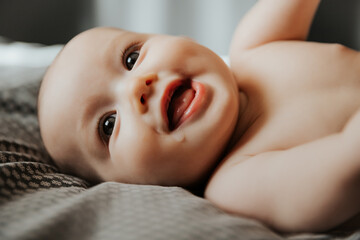 beautiful cute baby lying and playing on the bed in the room, photo with daylight from the window